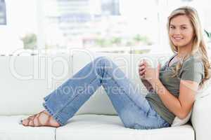 Woman sitting sideways on the couch, cup in hands, smiling and l