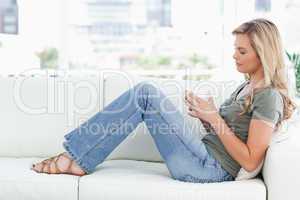 Woman sitting sideways on the couch, cup in hands, and eyes clos