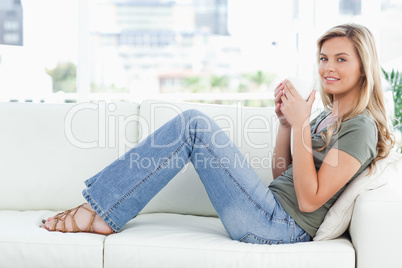 Woman sitting sideways on the couch, looking forward and cup rai