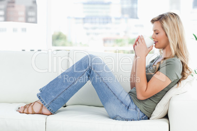 Woman sitting sideways on couch, cup raised up to her nose, eyes