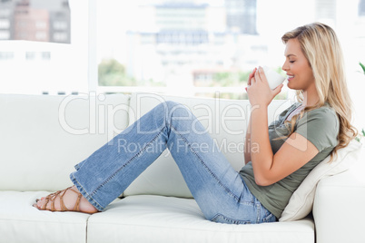 Woman smiling, with cup raised up to her nose and sitting sidewa