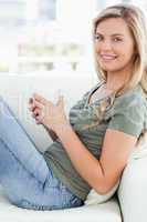 Close up, woman sitting across couch, cup in hands looking forwa