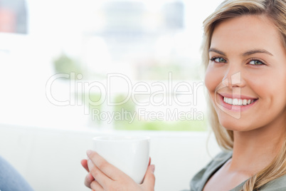 Woman smiling, looking forward and holding up a mug in hands