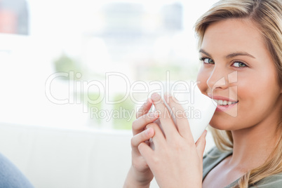 Woman smiling, holding a cup to her lips while looking forward