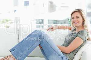 Woman sitting across couch, looking forward, smiling, and arm on