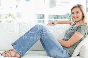 Woman sitting across the couch knees raised, smiling, looking fo