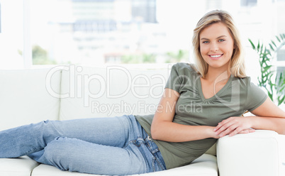Woman lying across the couch, looking forward, smiling with arms