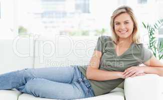 Woman lying across the couch, looking forward, smiling with arms