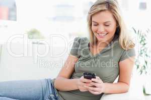 Woman smiles while using her phone and lying on the couch
