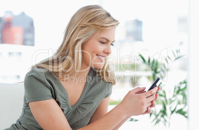 Woman smiles as she uses her phone while on the couch