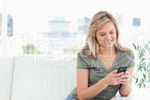 Woman sits on the couch, looking and using her phone and smiling