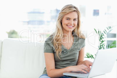 Woman smiling and looking forward as she uses a laptop on the co