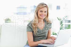 Woman smiling and looking forward as she uses a laptop on the co