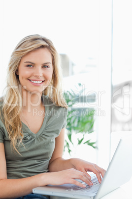 Woman smiling as she uses her laptop on the couch, side view