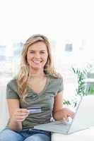 Woman using her credit card and laptop on the couch while smilin