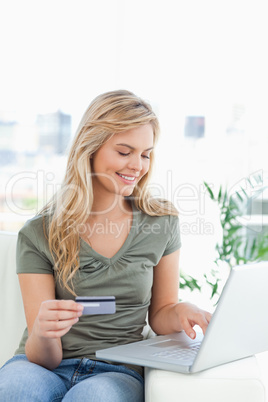 Woman smiles as she looks at her laptop with credit card in hand