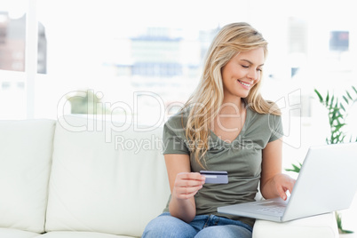 Woman smiles as she uses her laptop and credit card while sittin