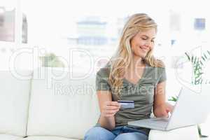 Woman smiles as she uses her laptop and credit card while sittin