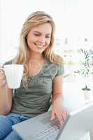 Woman smiling as she uses her laptop and holds a cup in her free