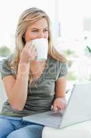 Woman taking a drink while using her laptop and looking to the s