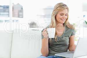 Woman smiling as she holds her cup and uses her laptop