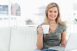 Woman looking forward and smiling as she uses her laptop and hol