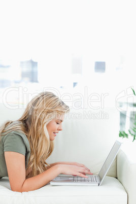 Close up, woman using laptop as she lies across couch