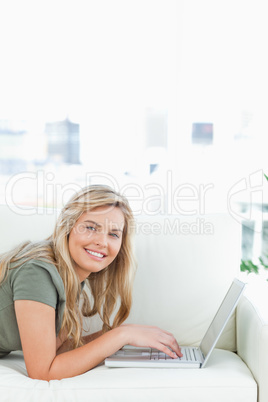Woman lying across the couch, looking foward and smiling and usi