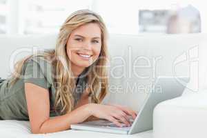 Woman lying across the couch with laptop in front of her, smilin