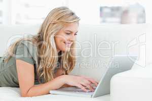 Woman smiling as she uses her laptop while lying across the couc