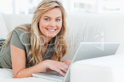Woman lying across the couch, smiling as she looks forward, usin