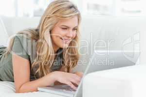 Woman lying across the couch using her laptop and smiling
