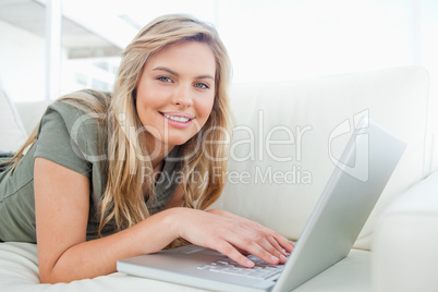 Woman looking ahead, smiling as she uses her laptop while lying