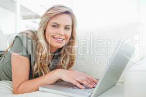 Woman looking ahead, smiling as she uses her laptop while lying