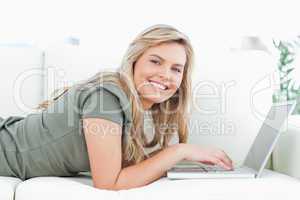 Woman lying on couch, using laptop and smiling