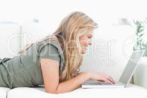 Woman using her laptop and smiling as she lies on the couch