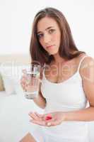 Woman with pills in one hand and a glass of water in the other l