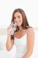 Woman smiles with a glass of water in hand raised to her mouth