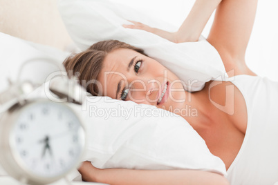Woman blocks her ears with a pillow as her alarm rings