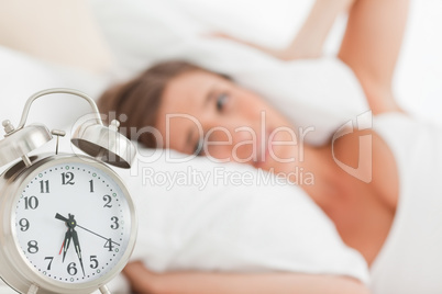 Woman with pillow over head head, as the alarm clock rings