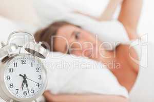 Woman with pillow over head head, as the alarm clock rings