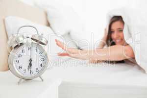 Woman under the quilt reaches for the clock