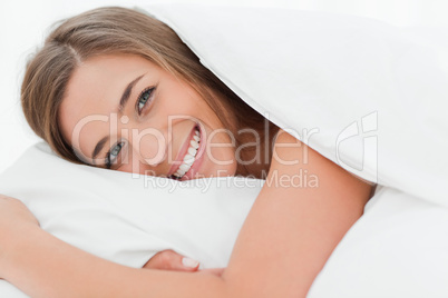 Close up, smiling woman in bed with her head on the pillow