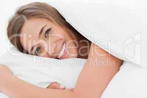 Close up, smiling woman in bed with her head on the pillow