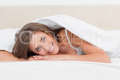 Woman smiling, while lying at the end of the bed, with head on h