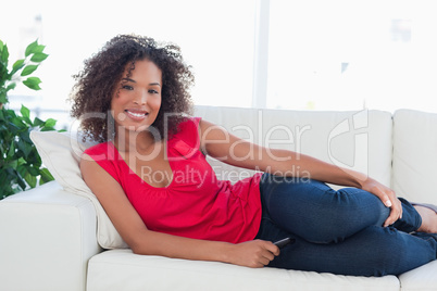 Woman on the couch looking forward and smiling with a phone in h