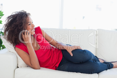 Woman lying on the couch making a call on her phone and smiling