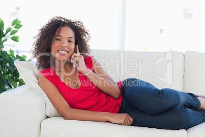 Woman on the couch, smiling while making a phone call and lookin