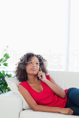 Woman making a call, while looking up, sitting on the couch