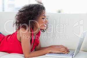 Woman smiling as she looks at and uses her laptop on the couch